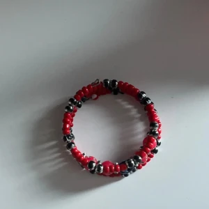 Rött pärlarmband med silverdetaljer - Unikt armband med röda och silvriga pärlor, dekorerat med glittriga rosa plattor och en blå pärla i mitten. Armbandet har en cool, rund form och är perfekt för dig som gillar färgstarka accessoarer med lite extra bling. Passar små händer eller barn 