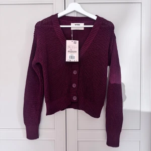 Mörkröd stickad kofta - Snygg mörkröd stickad kofta från STR med v-ringning och tre knappar framtill. Perfekt att slänga på över en t-shirt för en chill look.