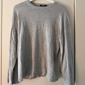 Grå finstickad tröja från Gina Tricot - En enkel och stilren grå stickad tröja från Gina Tricot i storlek M. Tröjan har rund halsringning, långa ärmar och ribbade muddar vid hals, ärmslut och nederkant. 