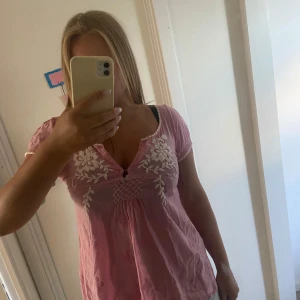 Rosa Odd Molly blus med broderi - Supersöt rosa blus från Odd Molly med vita broderade blommor och virkade detaljer vid halsringningen. Blusen har korta ärmar ich är v-ringad. Står inte storlek men passar S/M