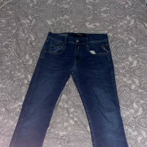 Replay blå jeans slim fit - Snygga blå jeans från Replay med klassisk femficksdesign och diskreta sömmar på bakfickorna. Modellen har slim fit och raka ben, med knapp och dragkedja framtill. Jeansen är gjorda i mjukt denimtyg som sitter skönt hela dagen.