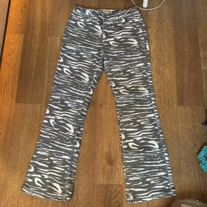 Gråmönstrade bootcut jeans från Guess - Säljer ett par gråa jeans från Guess med vitt zebramönster och bootcut-snitt. Byxorna har normal passform och klassisk femficksdesign. Perfekt för dig som vill sticka ut med coola mönster och snygg siluett.