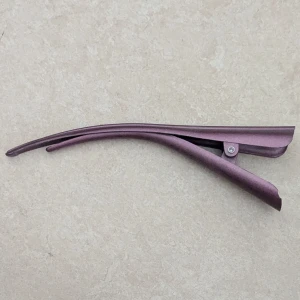 Lila hårklämma i plast  - Snygg lila hårklämma med smal och böjd design, perfekt för att fixa frisyren med stil. Klämman är gjord i plastl och har en enkel men cool look som passar till alla outfits. Enkel att använda och håller håret på plats hela dagen.