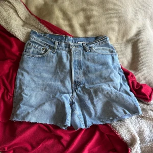 Levi's ljusblå jeansshorts hög midja - Ljusblå jeansshorts från Levi's med klassisk femficksdesign och rå kant nedtill. Hög midja och knappgylf, med Levi's patch och röd etikett bak. Perfekt för chill dagar och enkel att matcha med t-shirt eller hoodie.