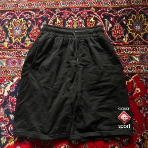 Casablanca Tennis Club Shorts - Svarta shorts från Casablanca Tennis Club med broderad logga 'casa sport' på vänster ben. De har elastisk midja med snörning, sidofickor och en bakficka. Mjukt bomullsmaterial som är skönt för chill eller sport. Klassisk loose passform.