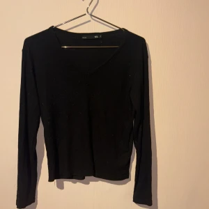 Svart ribbad tröja med v-ringning - En svart, ribbad långärmad tröja från 157 med snygg v-ringning. Tröjan har en enkel och clean design som passar perfekt till jeans eller kjol. Materialet är mjukt och stretchigt för en bekväm passform.