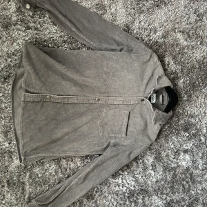 Grå manchesterskjorta från Zara - Säljer en grå manchesterskjorta från Zara med klassisk krage, bröstficka och knäppning framtill. Skjortan har lång ärm och är tillverkad i mjuk manchester med diskreta ränder. Perfekt för dig som gillar en chill och stilren look.