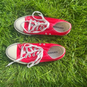 Röda Converse All Star sneakers - Klassiska röda Converse All Star sneakers med vit tå och sula, vita snören och tydliga kontrastsömmar. Lågt skaft och platt sula ger en tidlös look. Ovandel i canvas och detaljer i gummi. Perfekta för dig som gillar streetstyle och vill sticka ut.