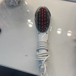 Fast Hair Straightener borste - Elektrisk hårborste som plattar håret snabbt. Borsten är vit med svarta borst och röda toppar, har digital display och knappar för temperaturkontroll. Perfekt för att fixa frisyren på nolltid. Sladd medföljer.