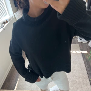 Svart Arket polotröja med ribbade detaljer - Säljer en svart polotröja med bred, ribbad krage och muddar. Tröjan har en loose passform och är långärmad, perfekt för dig som gillar en chill och enkel stil. Materialet känns stickat och mjukt mot huden, passar grymt till jeans eller kjol.