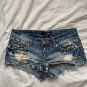 Blå jeansshorts från Tally Weijl - Snygga blå jeansshorts från Tally Weijl med slitna detaljer, fransig kant och coola nitar vid fickorna. Klassisk femficksmodell med låg midja och knappstängning. 