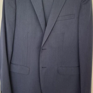 Blå kostym från Bläck Tailored Fit - Snygg blå kostym från Bläck med skräddad passform. Kavajen har klassiska slag, två framfickor med lock och bröstficka. Byxorna är matchande och har en stilren look. Perfekt för dig som vill ha en modern och stilren outfit. OBS: vuxenstorlek, passar mig som 189cm/86kg