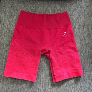 Rosa träningsshorts från Gymshark - Snygga rosa träningsshorts från Gymshark med hög midja och tight passform. Materialet är mjukt och stretchigt syntet, perfekt för gymmet eller löpning. Diskret Gymshark-logga på sidan och coolt mönstrad färgton som går från mörkare till ljusare rosa.