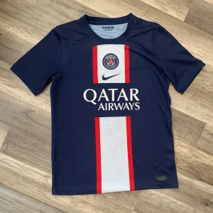 PSG tröja Mbappé 7 - Säljer en PSG tröja i barnstorlek L(140-160) skulle jag säga. Det är i ganska illa skick men är äkta. Fläcken syns på bild 4, det finns lite problem med tyget här och där som syns på bilderna igen.