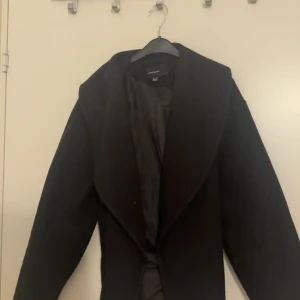 Svart kappa med knytskärp från Vero Moda - Stilren svart kappa från Vero Moda med knytskärp i midjan och bred krage. Jackan är långärmad och har en klassisk, rak passform. Perfekt för dig som vill ha en enkel men snygg look under höst och vinter. Materialet är mjukt och fodrat för extra komfort. Priset på kappan online är runt 700 spänn men vid kragen och ärmarna så har noppat sig något och släpper lite fibrer, (inget som påverkar användningen). Därför säljer jag kappan för ett bra pris. 