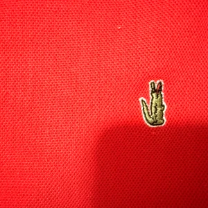 Röd Lacoste pikétröja i bomull - Säljer en klassisk röd pikétröja från Lacoste i storlek S. Tröjan har korta ärmar, krage och två knappar framtill. Ikoniska krokodilloggan är broderad på bröstet. Tillverkad i mjuk bomull som andas och passar perfekt till en avslappnad stil. Priset är inte fast.