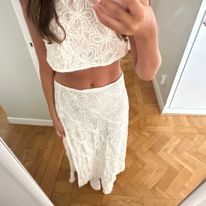 Vit set med blommigt mönster - Supersöt set från Musera i vit färg med broderade blommor över hela tyget. Kjolen har en slits på sidan och är gjord i ett lätt, luftigt material som passar perfekt till varma dagar. Båda plagg ingår tillsammans. Aldrig använd.