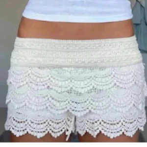 Spets shorts - Superfina vita shorts med bred midja och flera lager spetsvolanger. De har en feminin och bohemisk vibe med detaljerad spets och scallop-kant. Perfekta för varma dagar och ger en söt touch till din outfit.