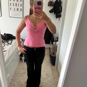 Rosa korsett-topp med rosett och cutout - Säljer en rosa korsett-topp med smala axelband, söt rosettdetalj framtill och en liten cutout under bysten. Toppen är croppad och har dragkedja i ryggen för enkel på- och avtagning. Perfekt för dig som vill sticka ut med en färgglad och trendig look.