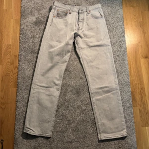 Levi's 501 ljusgrå jeans W29 L30 - Säljer ett par klassiska Levi's 501 jeans i en snygg ljusgrå tvätt. Jeansen har raka ben, fem fickor och knäppning fram. Perfekt för dig som gillar en tidlös och clean look. Passar både street och casual vibes.