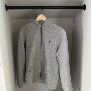Grå hoodie från Polo Ralph Lauren - Säljer en grå hoodie från Polo Ralph Lauren i storlek 18-20 (xs). Tröjan har dragkedja framtill, huva och två fickor. Klassisk logga broderad på bröstet. Perfekt för chill dagar och enkel att matcha med jeans.