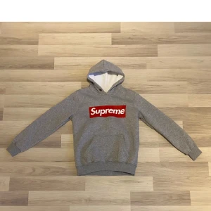 SUPREME GE OFFER! - GE OFFER.       DEN E L FAST PASSAR M Supreme hoodie i grått med den klassiska röda boxloggan framtill. Tröjan har huva med vit insida, magficka och ribbade muddar vid ärmar och nederkant. Perfekt för dig som gillar streetwear och vill sticka ut med en ikonisk look.
