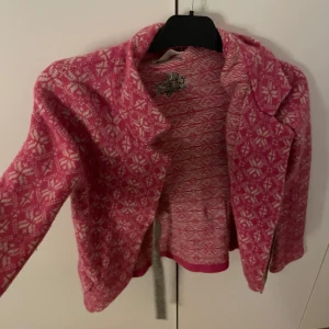 Rosa stickad cardigan jacka Odd Molly - Superfin rosa och vit stickad cardigan jacka från Odd Molly med snyggt mönster och broderad detalj på bröstet. Jackan har krage, långa ärmar och är gjord i mjuk ullmix. Perfekt för dig som vill ha något färgglatt och unikt i garderoben!