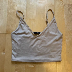 Beige linnetopp från Amisu - Säljer en stilren beige linnetopp från Amisu med smala axelband och v-ringad hals. Toppen är croppad och har en enkel, clean look som är lätt att matcha med allt. Perfekt för varma dagar eller lager på lager.