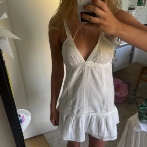 Vit kort sommarklänning från bikbok OANVÄND - Supersöt vit klänning från bikbok med v-ringad front och axelband. Klänningen har en volang nedtill och är tillverkad i mjuk bomull, perfekt för varma dagar. Den är kort och har en lätt och luftig känsla, med en enkel men chic design som är lätt att matcha.