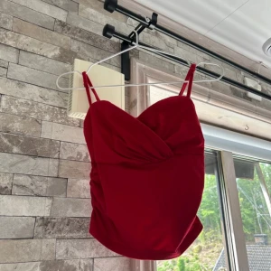 Röd omlott linnetopp med smala band - Snygg röd linnetopp med omlottdesign och smala axelband. Toppen har en figurnära passform och lätt rynkade sidor som ger en cool siluett. Perfekt för dig som vill sticka ut med en färgstark look.