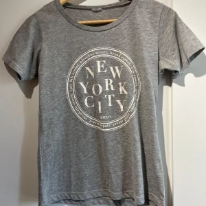 Grå t-shirt med New York City-tryck - Snygg grå t-shirt med rund hals och korta ärmar. Har används en del men är i gott skick💞