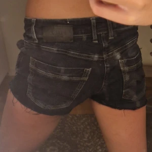 Mörkblå jeansshorts från Pulz Jeans - Snygga mörkblå jeansshorts från Pulz Jeans med råa kanter och klassiska fickor både fram och bak. Shortsen har normal passform, midja med hällor och knäppning framtill. Perfekta för sommaren och ger en cool, avslappnad vibe.