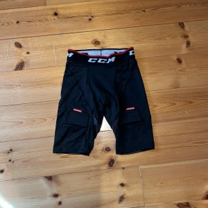 Svarta CCM träningsshorts S - Svarta träningsshorts från CCM med elastisk midja och röda detaljer. Shortsen har praktiska kardborrefästen på benen fram och bak och är tillverkade i ett lätt syntetmaterial som andas. Nypris 599kr.