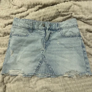 Ljusblå jeanskjol  - Säljer en ljusblå jeanskjol med slitna detaljer. Kjolen har klassiska fickor fram och bak, samt snygga broderade bakfickor med rosa sömmar. Jätte snygg och skön , passar till allt . Barn storlek från ginas young edition. Sitter som en xs.