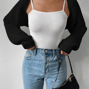 Svart croppad stickad väst från SHEIN - Svart croppad stickad väst från SHEIN i storlek S. Modellen har långa ärmar och är ribbstickad för en cool och trendig look. Perfekt att slänga över ett linne eller t-shirt för att få till en snygg layering-effekt.