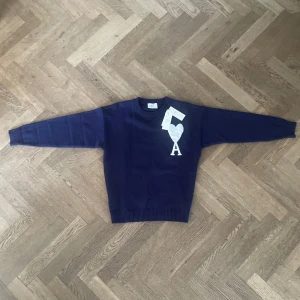Ami Paris tröja  - Säljer en marinblå stickad tröja från Ami med ett stort vitt hjärta och bokstaven A på bröstet. Tröjan har rund hals, ribbade muddar och långa ärmar. Perfekt för dig som gillar stilrena detaljer och vill ha något som sticker ut lite extra. Passar runt 180