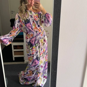 Lång färgglad mönstrad klänning - Säljer en set kjol och topp med lila, rosa, gul och blå färger i ett unikt blommigt och abstrakt mönster. Överdelen är långärmadeoch har resår vid handlederna och kjol har elastisk resår i midjan . Materialet är mjukt och faller snyggt, perfekt för dig som gillar färg och statement-plagg.Helt ny