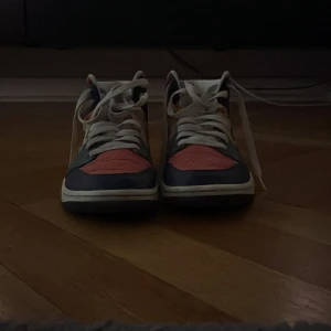 Nike Air Jordan 1 färgglada sneakers - Säljer ett par Nike Air Jordan 1 sneakers i en riktigt färgstark mix av rosa, blått, rött, vitt och gult. Skorna har klassisk snörning, vit sula och den ikoniska Air Jordan-loggan på sidan. Perfekta för dig som vill sticka ut med din stil.