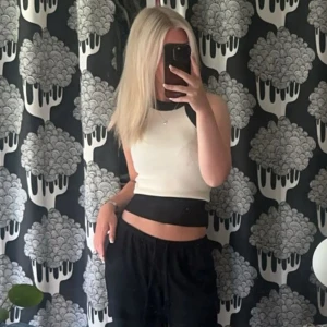 Vit och svart topp - Säljer en snygg croppad linnetopp i vitt med svarta detaljer vid halsringning och midja. Toppen är ärmlös och har en tight passform som framhäver midjan. Perfekt för dig som gillar en stilren och sportig look.