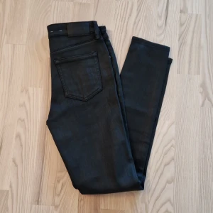 Helt nya svarta shiny skinny jeans från Lauren Ralph Lauren - Snygga svarta jeans från Lauren Ralph Lauren med klassisk femficksdesign och smal passform. Jeansen har midja med hällor, dragkedja och knapp framtill. Perfekta för dig som gillar stilrena och tidlösa plagg.