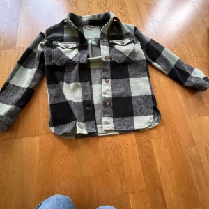 Rutig overshirt från H&M i svart och grått - Snygg rutig overshirt från H&M i svart och grått med stora rutor. Skjortan har två bröstfickor med knappar, klassisk krage och långa ärmar. Perfekt att slänga över en t-shirt.                 Om du vill ha fler bilder är det bara att säga till🤗