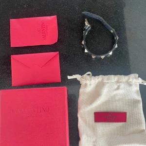Valentino Garavani mörkblå  - Snyggt svart armband från Valentino Garavani med coola pyramidformade nitar i guld. Justerbart spänne och exklusiv känsla. Kommer med originalförpackning och dustbag med extra spikar och ett brev. Perfekt accessoar för att lyfta din outfit.