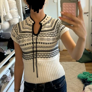 Vit och svart stickad topp från Zara - Säljer en snygg stickad topp från Zara i vitt och svart med korta ärmar och coolt grafiskt mönster. Den har snörning vid halsen och ribbad midja som ger en schysst passform. Perfekt för dig som gillar unika detaljer och vill sticka ut lite extra.