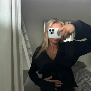 Svart långärmad blus med v-ringning från Gina - Säljer en svart långärmad blus från Gina Tricot med v-ringning och markerad midja med resår. Blus har en elegant och enkel design, perfekt för dig som gillar stilrena plagg. Materialet känns mjukt och har en lätt glans.