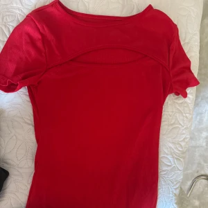 Röd ribbad topp med cut-out - Snygg röd ribbad topp med korta ärmar och cool cut-out detalj vid halsen. Perfekt för dig som vill sticka ut med en färgstark look. Materialet är mjukt och stretchigt, vilket gör den skön att bära. Passar dig som gillar trendiga och enkla plagg.