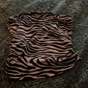Kortkjol med rosa zebramönster - Säljer en kortkjol med riktigt snyggt zebramönster i svart och ljusrosa. Kjolen har en rak och enkel form, perfekt för dig som vill sticka ut med ett coolt djurmönster. Materialet känns mjukt och följsamt mot huden. Passar dig som gillar att vara trendig och våga lite mer.