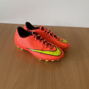 Nike Mercurial orange fotbollsskor - Säljer ett par Nike Mercurial fotbollsskor i en riktigt snygg orange färg med gula och svarta detaljer. Skorna har snörning och platt sula med gula dobbar för gräsplan. Ovandelen är i syntetmaterial och har en smal, sportig form. Perfekt för dig som vill sticka ut på planen. Änvända i cirka 1 år pris kan diskuteras 