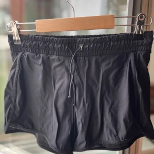 Svarta badshorts med snörning - Snygga svarta badshorts med elastisk midja och snörning framtill. De har inbyggde bikini trosor.