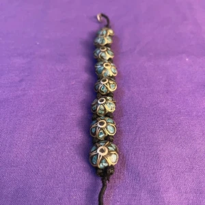 Armband med blommönster - Knutet armband. Pärlorna och hela armbandet är handgjort och de har målats som blommor i turkos och guld. 19 cm långt