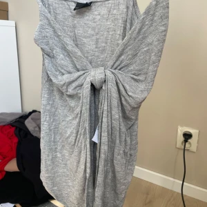 Grå tröja med knyt från Gina Tricot - Säljer en snygg grå korttröja från Gina Tricot i mjukt bomullsmaterial.Tröjan har ett coolt knyt framtill som ger en unik look och är ärmlös för en fräsch vibe. Perfekt för dig som gillar stilrena och enkla plagg med en twist.